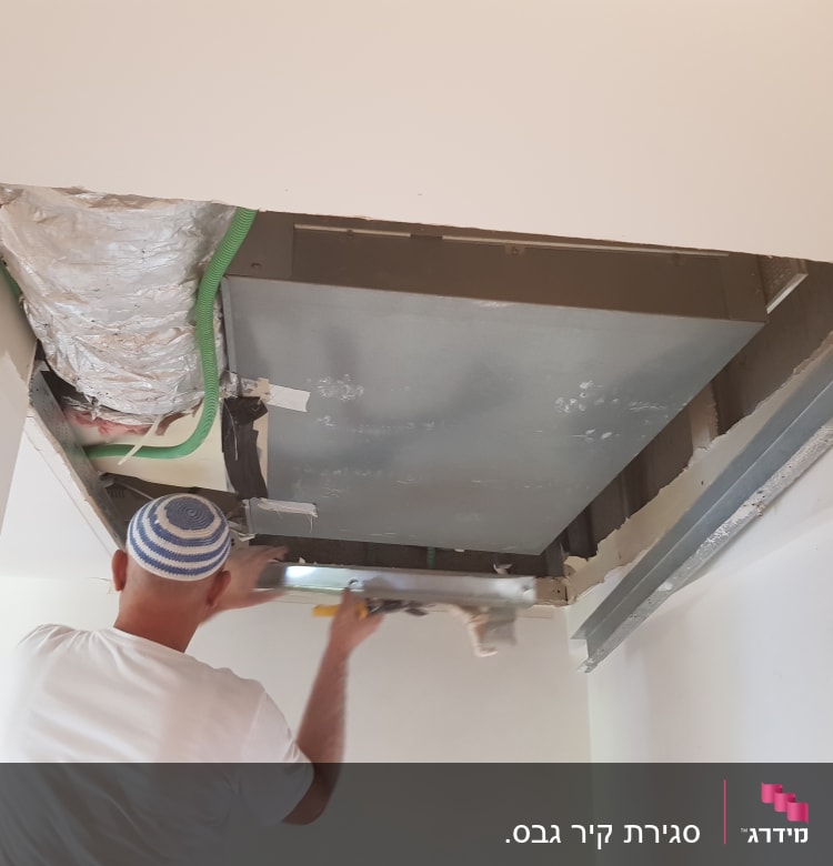 אדם עובד על תקרת גבס עם כלי עבודה